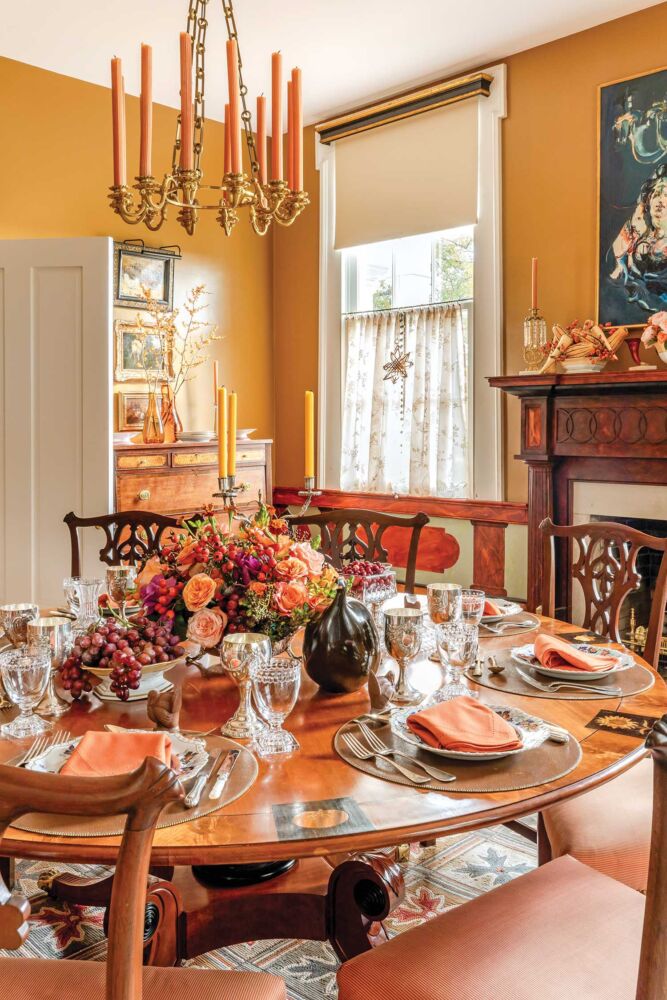 A round wooden table holds place settings and a coral floral center in a gold painted dining room.