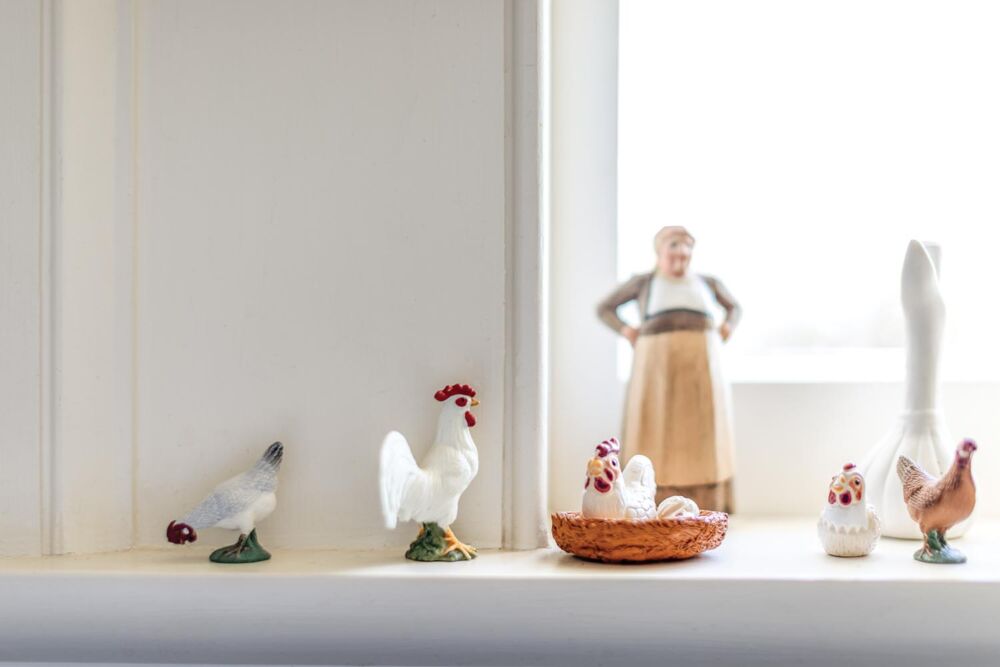 Tiny ceramic chicken figurines sit lit by morning light on a window sill.