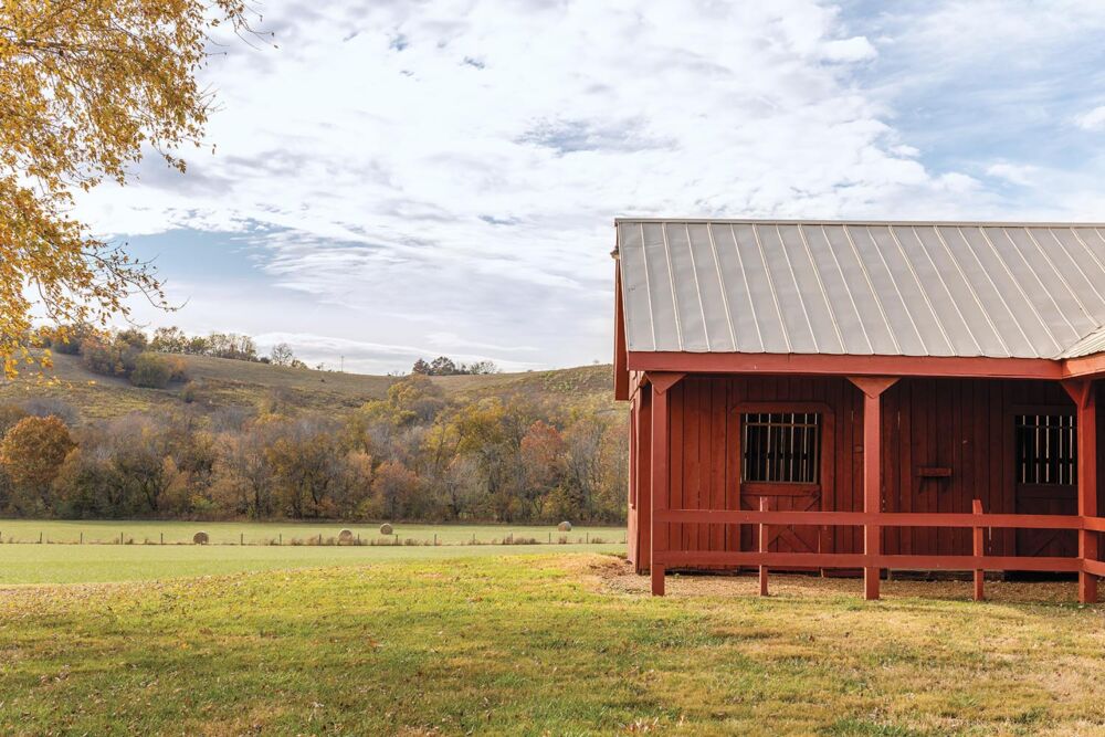 A red barn sits on a large meadow with rolling hills in the background.