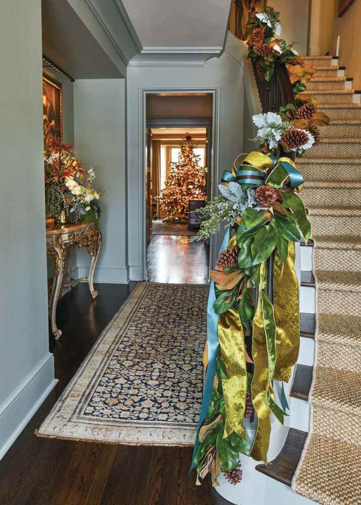 Olive green and turquoise ribbon are tied in ribbons with pinecones and magnolia leaves at the bottom of a staircase.