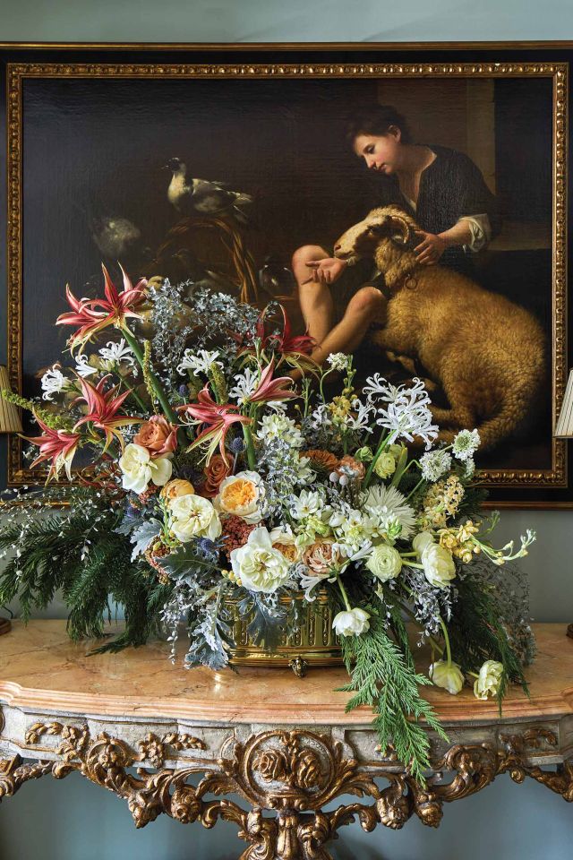 Assorted amaryllis, nerines, garden roses, and ranunculus form an arrangement in front of a 17th century Italian painting.