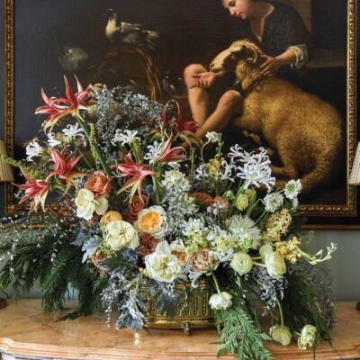 Assorted amaryllis, nerines, garden roses, and ranunculus form an arrangement in front of a 17th century Italian painting.