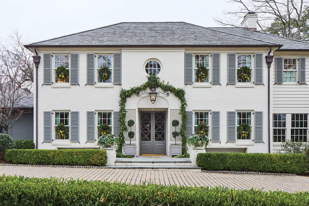 A two-story white colonial house is decorated in greenery for Christmas.