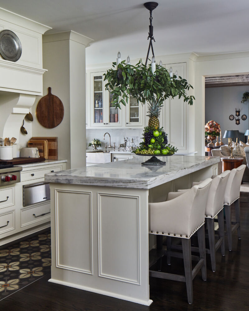 A white kitchen has a hanging chandelier covered in greenery.