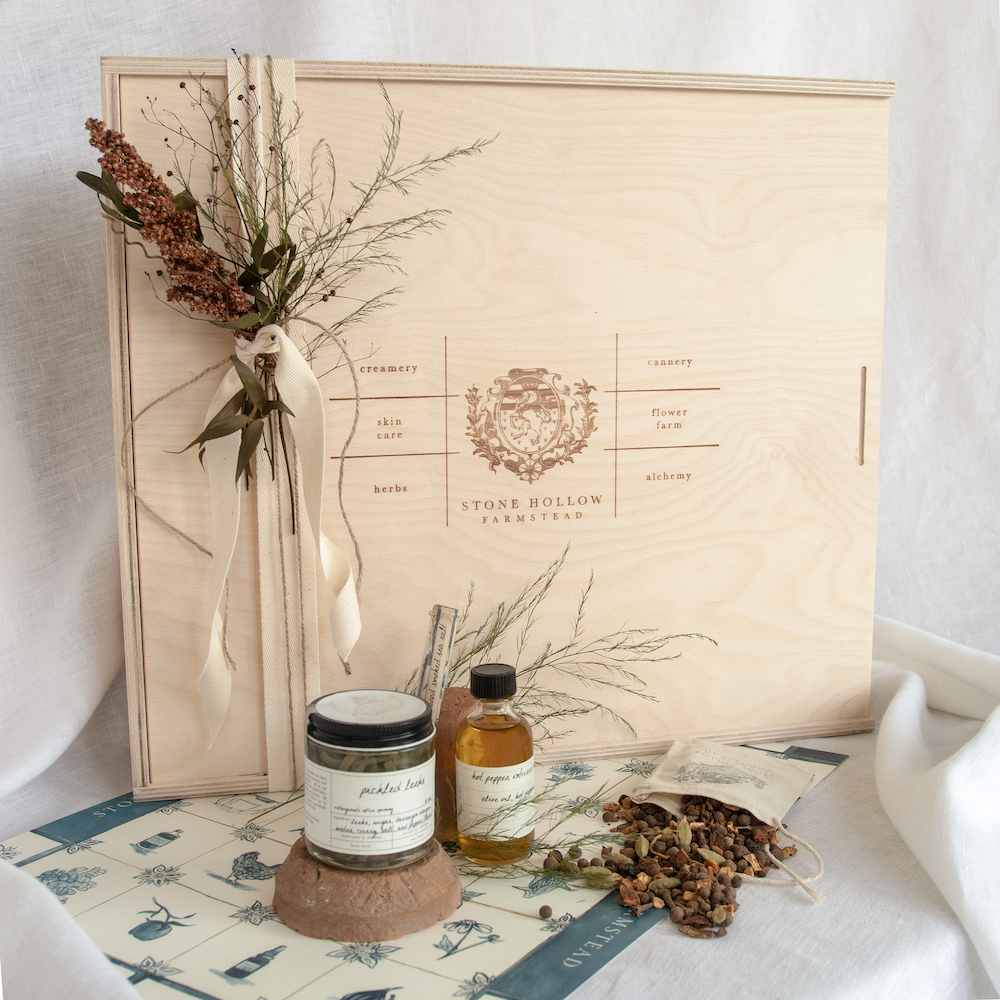 A wooden box has dried florals ribboned on top next to jams, jellies, and potpourri.
