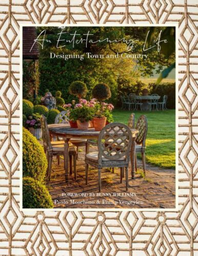 And outdoor table with boxwoods sits in sunset life on the cover of AN ENTERTAINING LIFE.