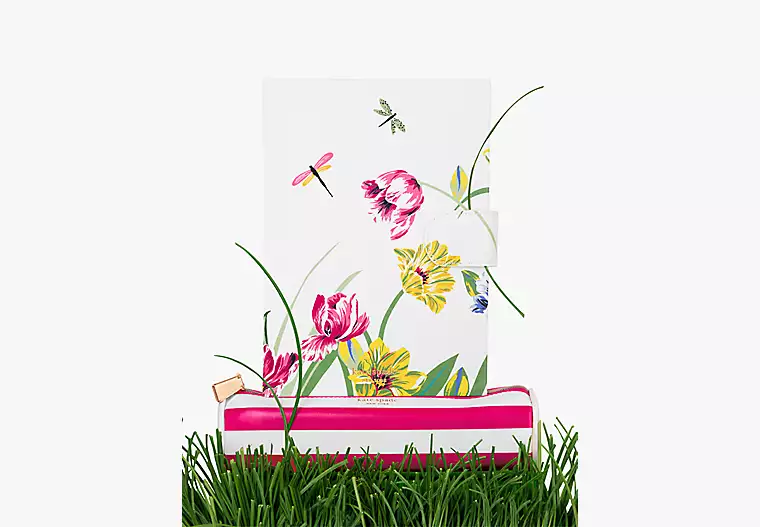 A floral notebook with butterflies and dragonflies sits on green grass.
