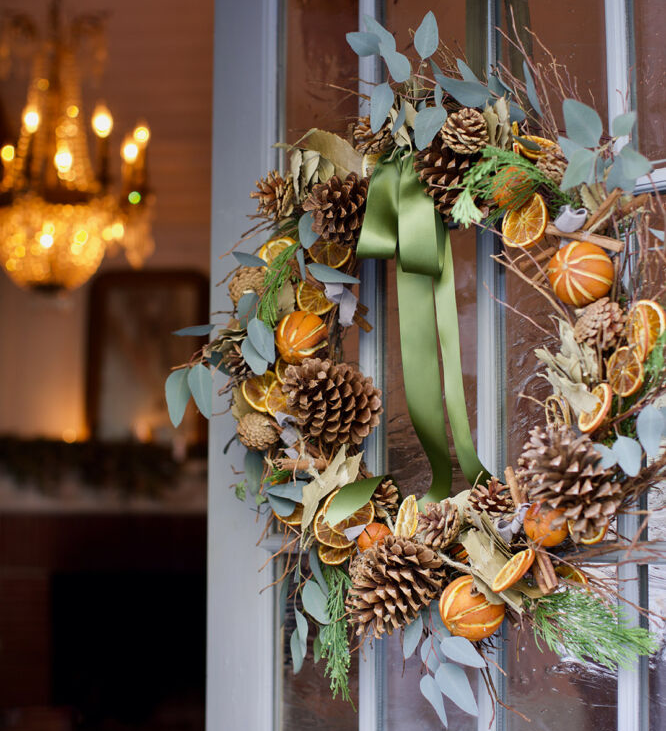 Dried citrus wreath with green ribbon, pine cones, and fragrant eucalyptus hanging on door.