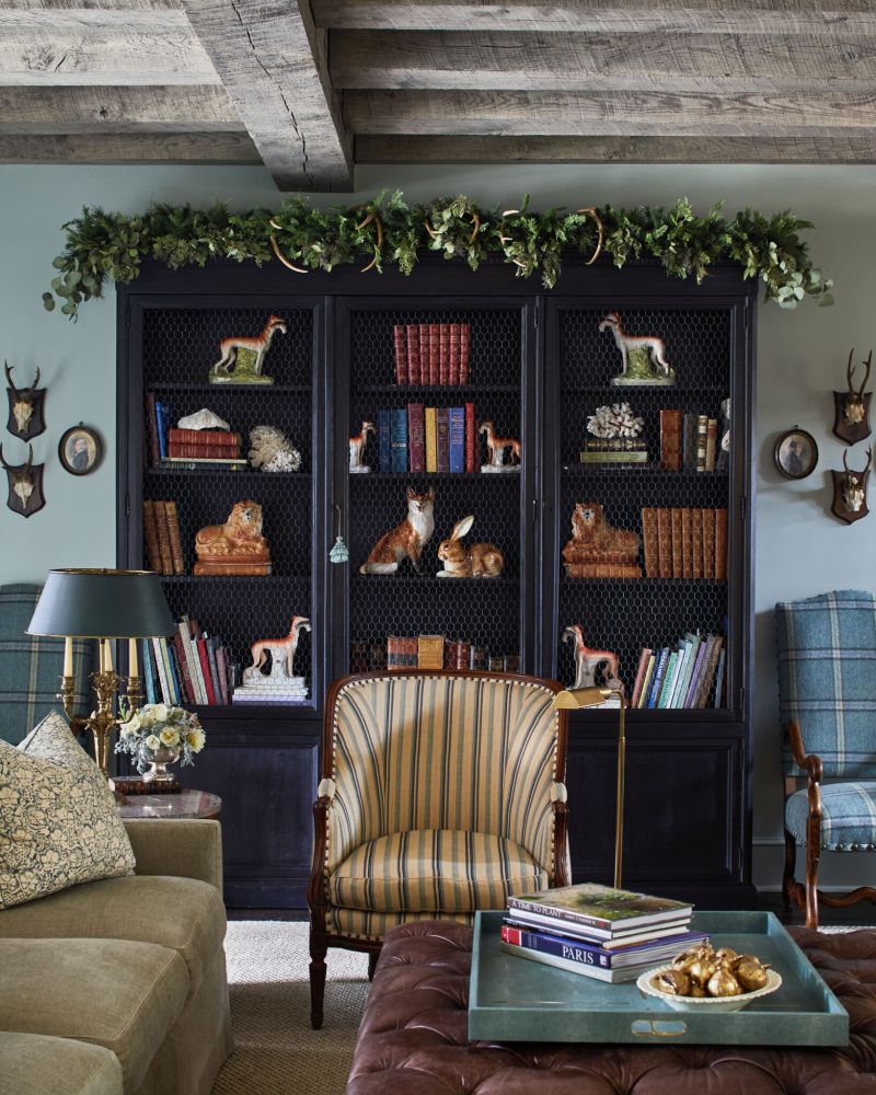 A black bookcase has festive greenery on top.
