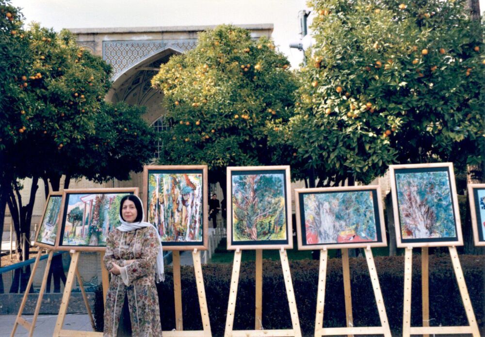 Laurie Blum stands with her paintings and orange trees behind her.