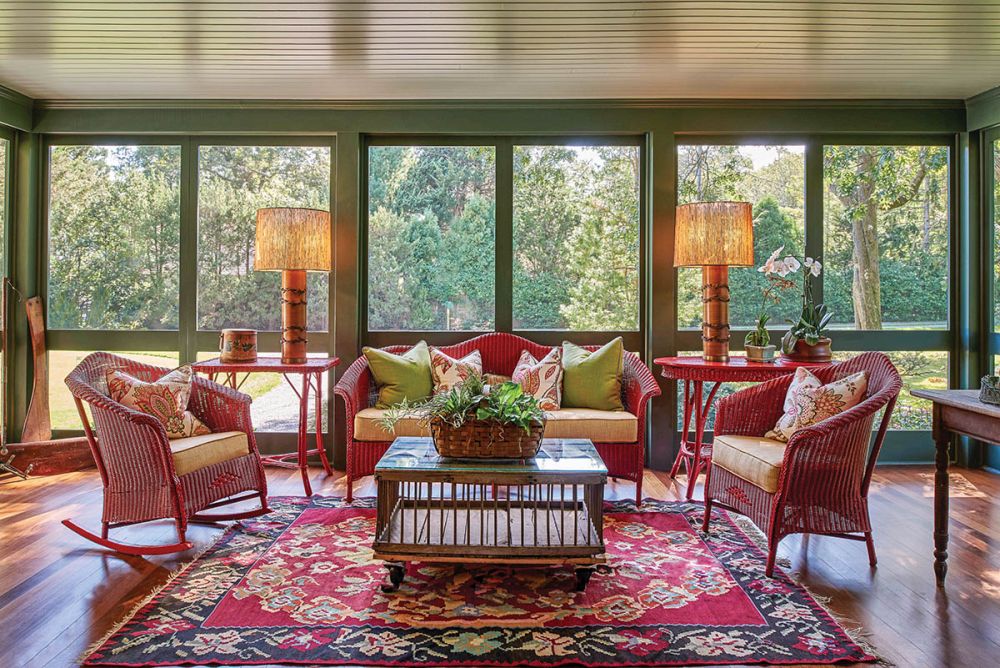 Red furniture accents a green screened porch.