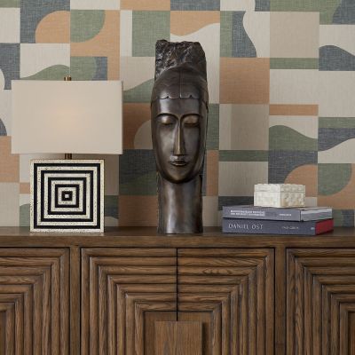 Large bust, graphic black and white square lamp, stack of books and a box atop a wooden chest or credenza.