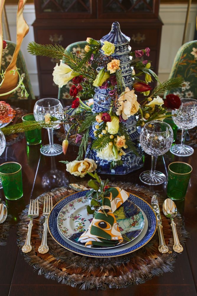 A blue and white tulipiere overflows with flowers at a Christmas table.
