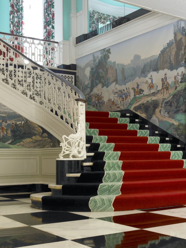 Lower lobby staircase at the Greenbrier Hotel with scenic wallpaper.