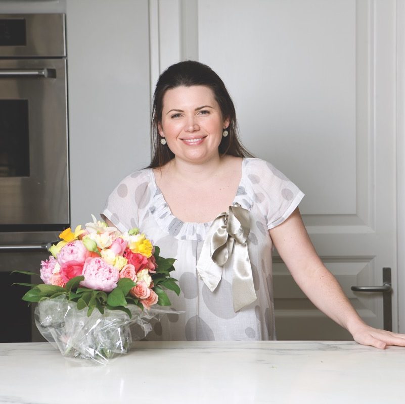 Phoebe stands next to a kitchen island with a colorful bouquet of roses.