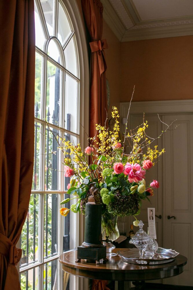 A large bouquet of forsythia and roses next to an arched window.