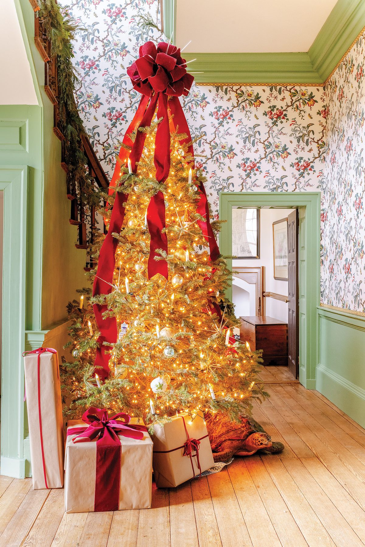 A brightly lit Christmas tree stands in a wallpapered hallway.