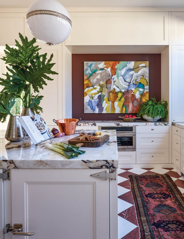 A white kitchen with contemporary art, a Turkish rug, and checkerboard flooring.