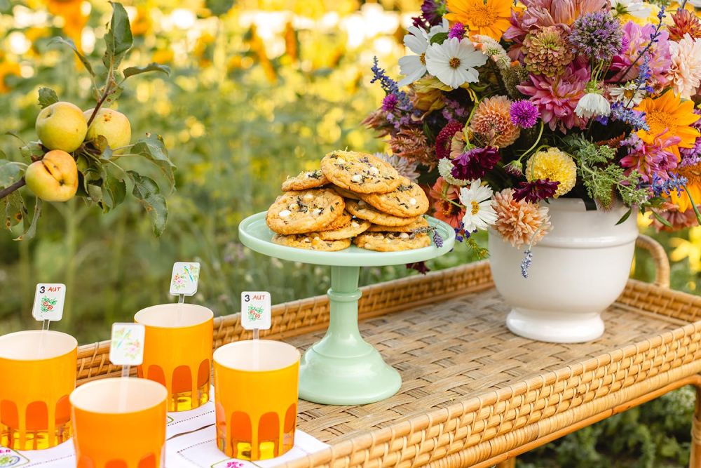 White chocolate chip cookies on a teal cake stand next to a bouquet of flowers.