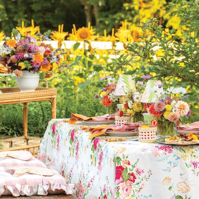 A table is set with a floral tablecloth, flowers, and orange and pink napkins.