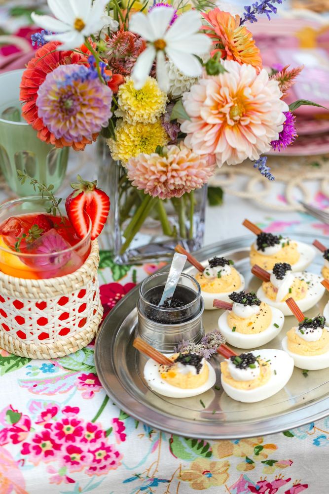 A floral bouquet sits on a table behind deviled eggs topped with caviar.