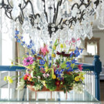 Multicolored wild flowers in a wide arrangement under a chandelier.
