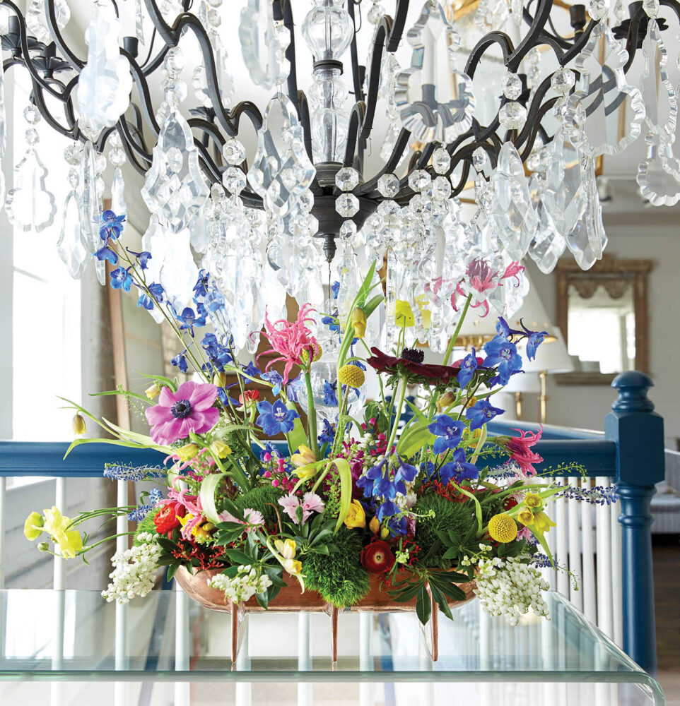 Multicolored wild flowers in a wide arrangement under a chandelier.
