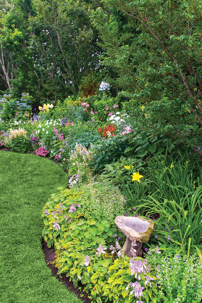 A blooming garden curves around a patch of grass.
