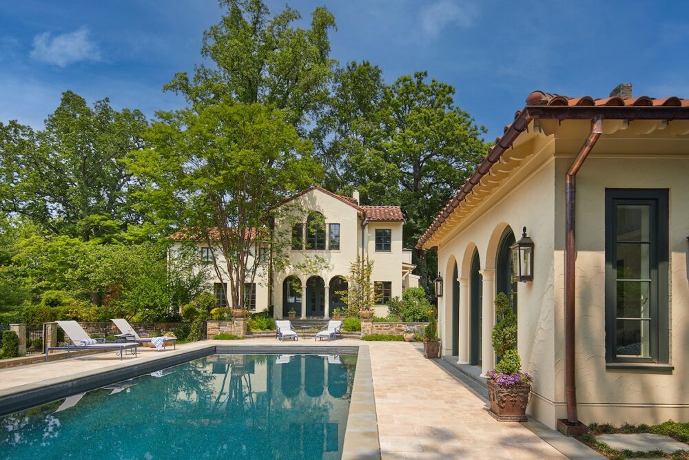 The new pool and pool house slips gracefully into the landscape and reflects the exterior of the original house, including perfectly matched stucco, red tile roof, and arched detailing.