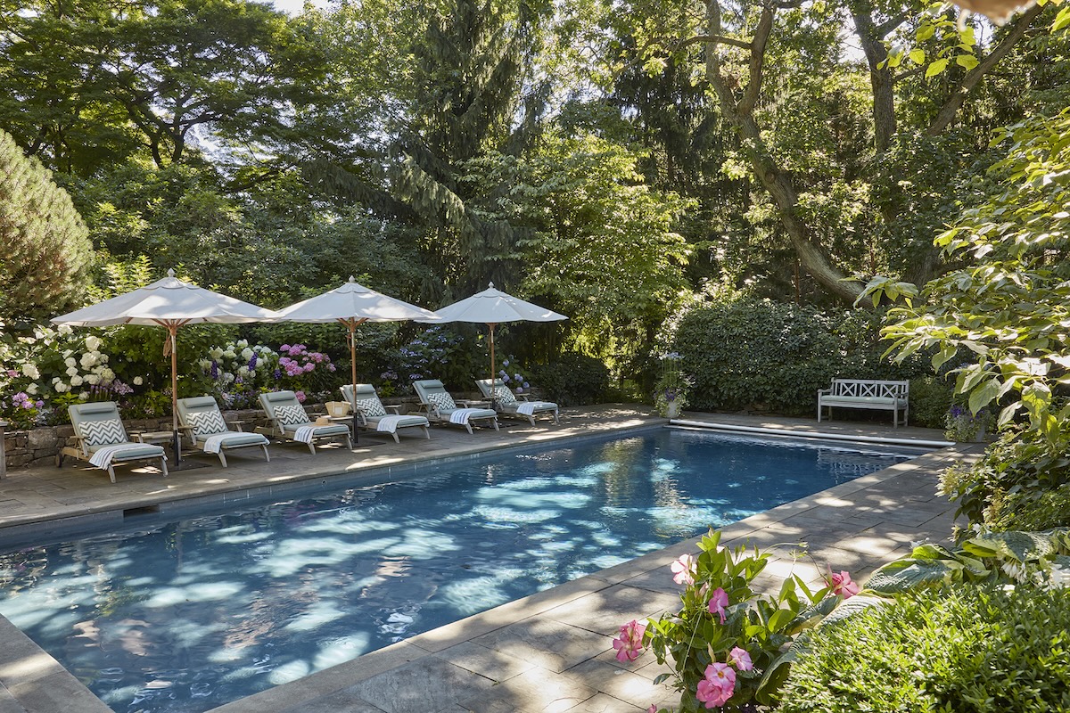 Pool with line of lounges and umbrellas in dappled sunlight.
